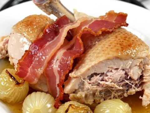 A top-down view of chicken thighs, bacon, and pearl onions cooking in a slow cooker.