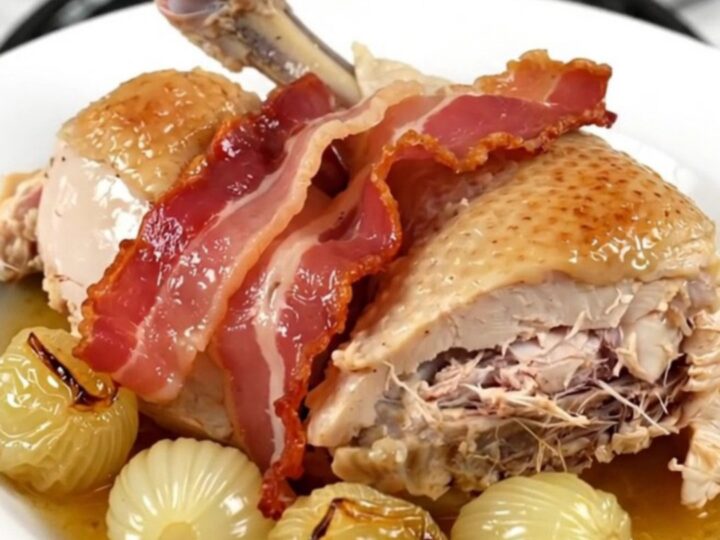 A top-down view of chicken thighs, bacon, and pearl onions cooking in a slow cooker.