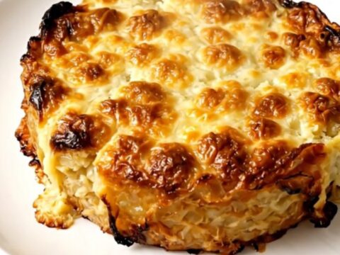 A top-down view of a creamy potato gratin inside a black slow cooker on a white speckled countertop.
