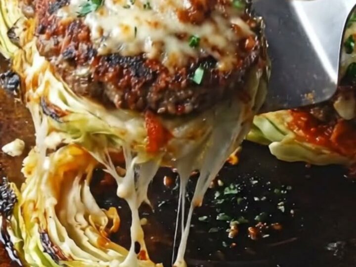 Cheesy beef-stuffed cabbage steaks on a dark baking sheet, garnished with parsley.