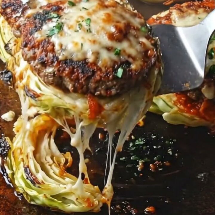 Cheesy beef-stuffed cabbage steaks on a dark baking sheet, garnished with parsley.