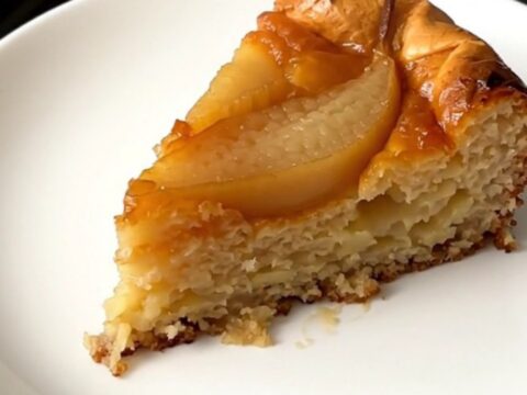A warm slice of pear clafoutis on a white plate with a golden, set custard texture.