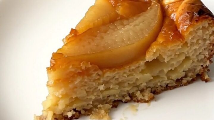 A warm slice of pear clafoutis on a white plate with a golden, set custard texture.