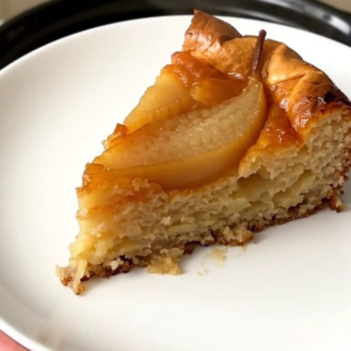 A warm slice of pear clafoutis on a white plate with a golden, set custard texture.