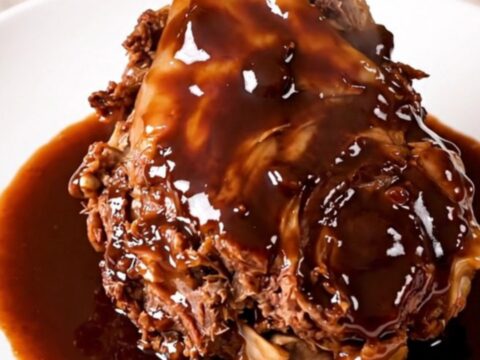 Two tender lamb shanks in a rich, dark red wine sauce with shallots on a white plate.