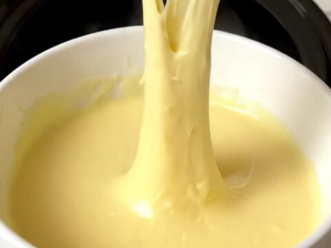 A slow cooker filled with creamy, melted three-cheese fondue on a speckled quartz countertop.