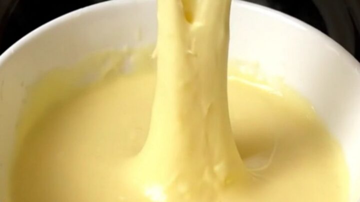 A slow cooker filled with creamy, melted three-cheese fondue on a speckled quartz countertop.