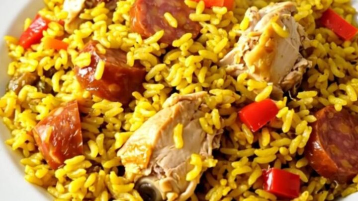 A top-down view of a black slow cooker filled with chicken, chorizo, and red peppers on a white speckled countertop.