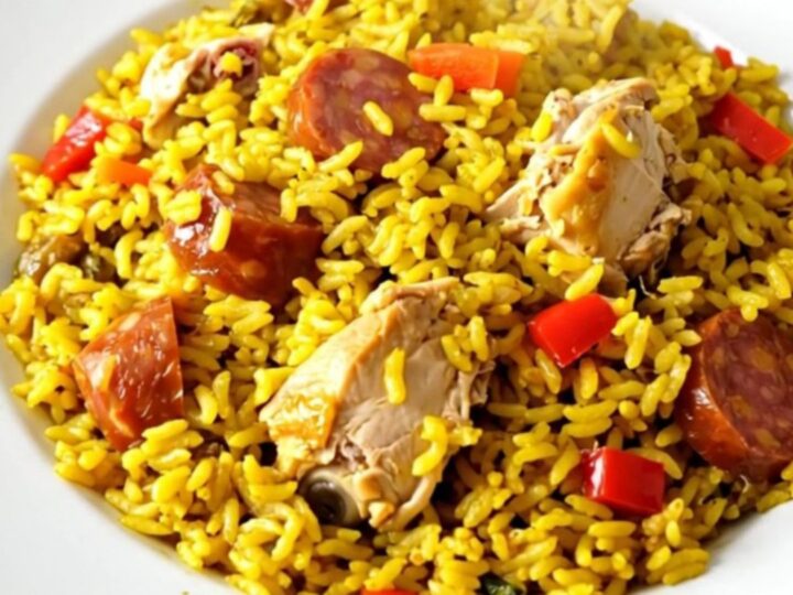 A top-down view of a black slow cooker filled with chicken, chorizo, and red peppers on a white speckled countertop.
