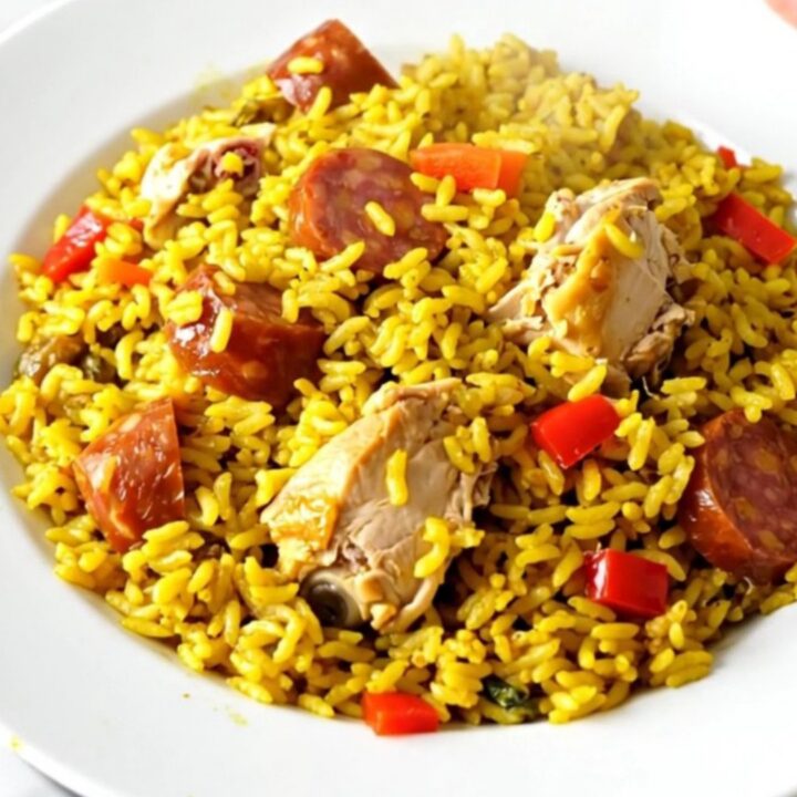 A top-down view of a black slow cooker filled with chicken, chorizo, and red peppers on a white speckled countertop.