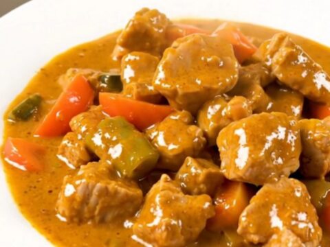 A steaming bowl of slow-cooked coconut pork curry with chunks of tender pork and carrots in a creamy sauce.