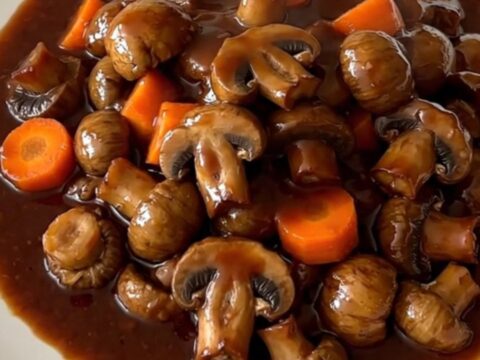 A top-down view of a black slow cooker filled with mushroom bourguignon on a speckled countertop.