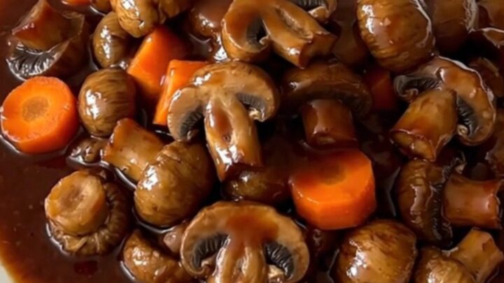 A top-down view of a black slow cooker filled with mushroom bourguignon on a speckled countertop.