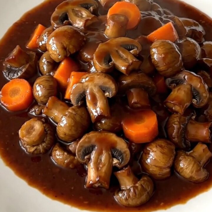 A top-down view of a black slow cooker filled with mushroom bourguignon on a speckled countertop.