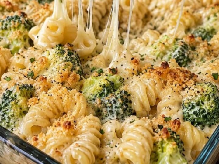 A close-up of a spoon lifting cheesy, creamy rotini pasta and tender broccoli florets from a baking dish.