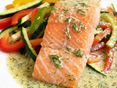 A top-down view of raw salmon fillets topped with julienned vegetables and dill in a slow cooker.