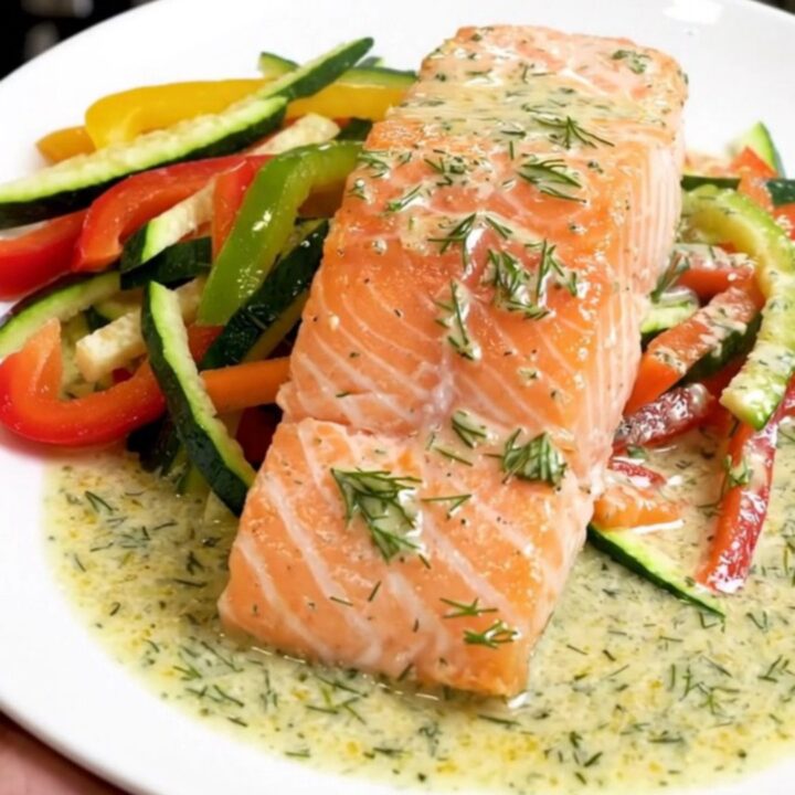 A top-down view of raw salmon fillets topped with julienned vegetables and dill in a slow cooker.