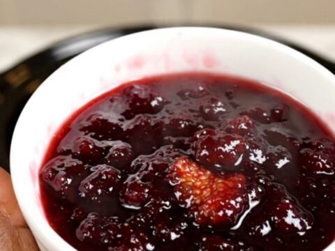 A bowl of rich, dark purple fig and honey jam served on a white plate with a spoon.