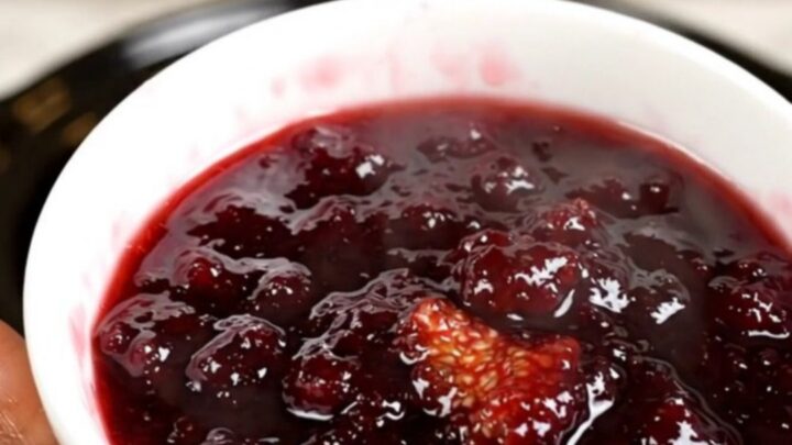 A bowl of rich, dark purple fig and honey jam served on a white plate with a spoon.