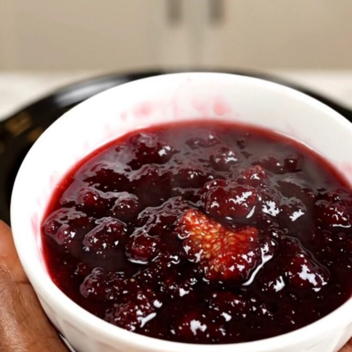 A bowl of rich, dark purple fig and honey jam served on a white plate with a spoon.