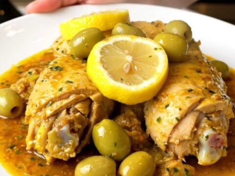 Tajine de poulet aux citrons confits et olives servi dans une assiette blanche, vue de dessus avec vapeur.