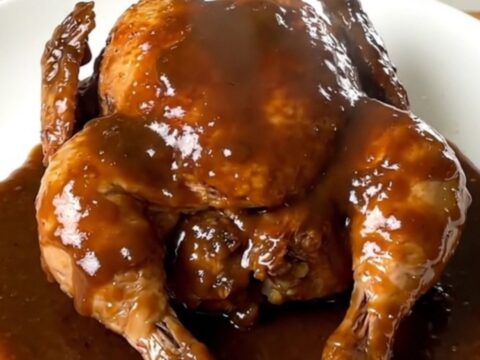 A close-up shot of slow-cooked chicken legs with a glossy beer gravy on a white plate.