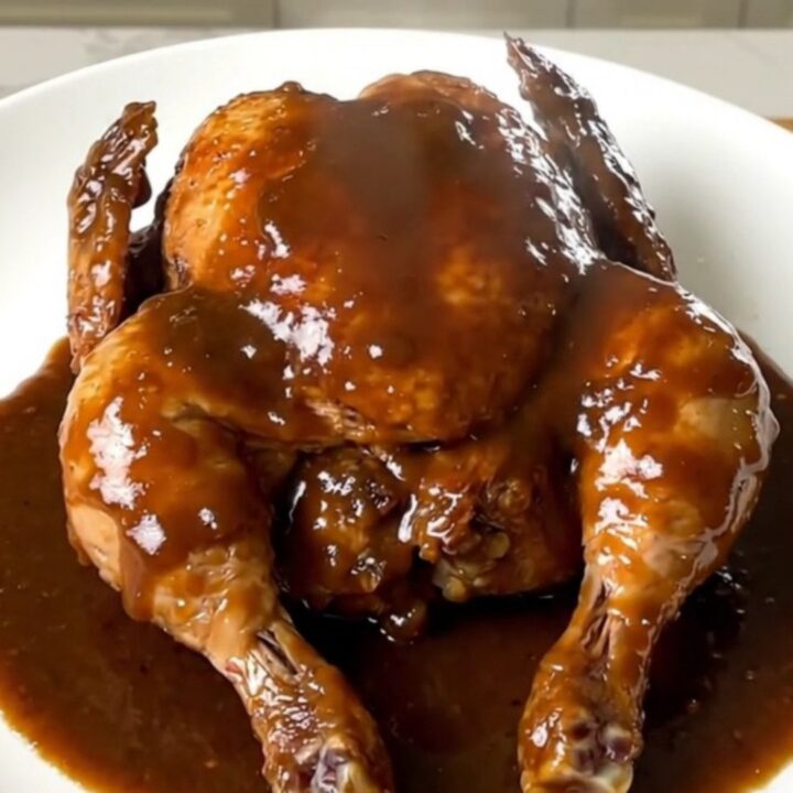 A close-up shot of slow-cooked chicken legs with a glossy beer gravy on a white plate.