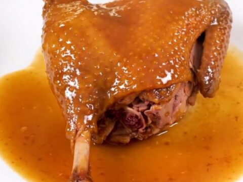 A finished slow cooker duck leg with an amber orange glaze on a white plate.