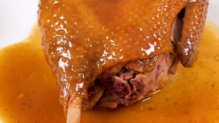 A finished slow cooker duck leg with an amber orange glaze on a white plate.