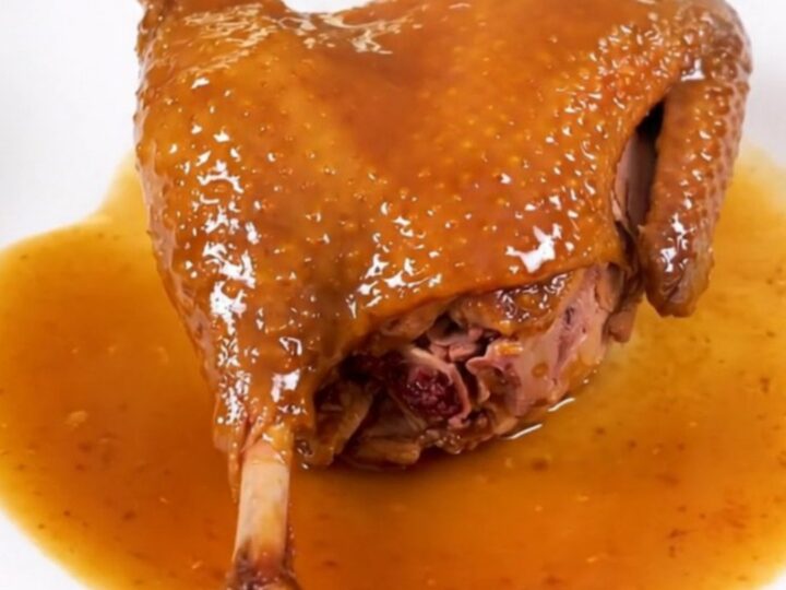 A finished slow cooker duck leg with an amber orange glaze on a white plate.