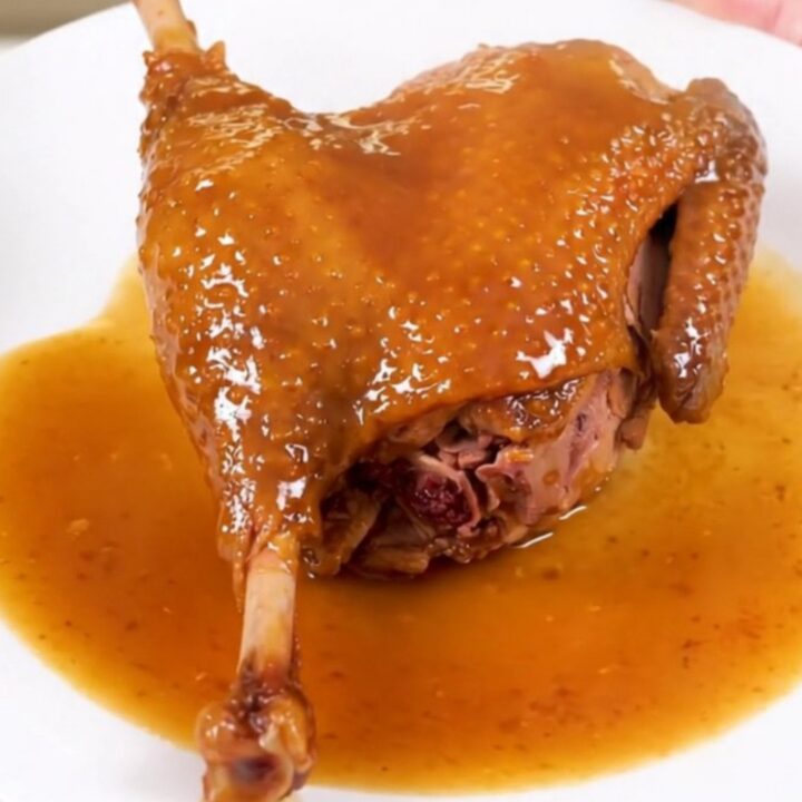 A finished slow cooker duck leg with an amber orange glaze on a white plate.