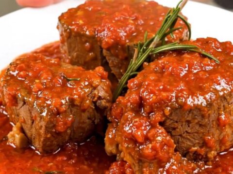 A close-up of tender, slow-cooked veal shanks in a rich tomato sauce garnished with fresh rosemary on a white plate.