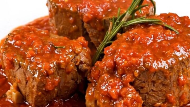 A close-up of tender, slow-cooked veal shanks in a rich tomato sauce garnished with fresh rosemary on a white plate.