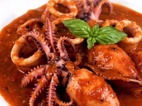 A top-down view of raw cuttlefish, sliced onions, garlic, and tomato sauce in a slow cooker insert.