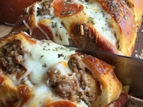 A close-up shot of a golden-brown braided pizza bread sliced on a wooden board with melted cheese and beef visible.
