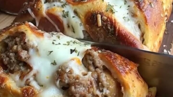 A close-up shot of a golden-brown braided pizza bread sliced on a wooden board with melted cheese and beef visible.