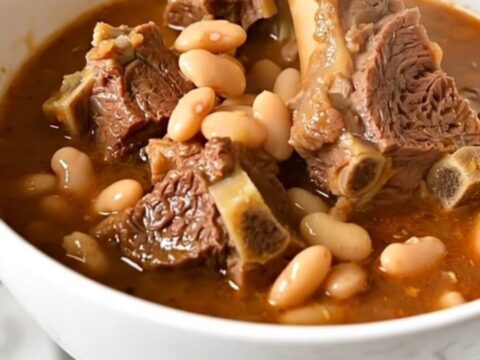 A top-down view of raw lamb cubes, white beans, and tomatoes in a slow cooker, ready to be cooked.