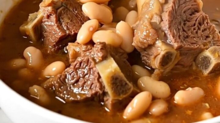 A top-down view of raw lamb cubes, white beans, and tomatoes in a slow cooker, ready to be cooked.