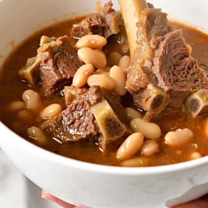 A top-down view of raw lamb cubes, white beans, and tomatoes in a slow cooker, ready to be cooked.