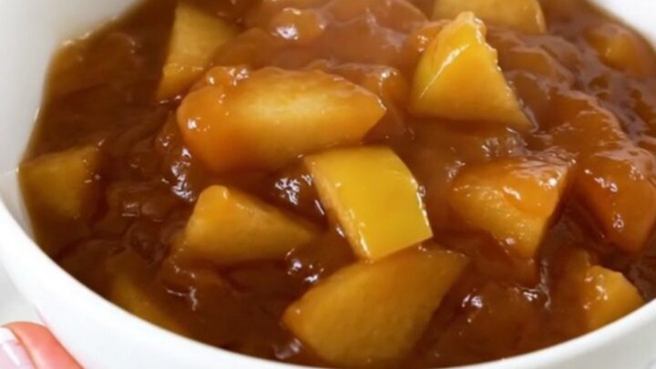 A white bowl filled with glossy, cooked quince and apple compote, showing soft, tender fruit pieces and a rich syrup.