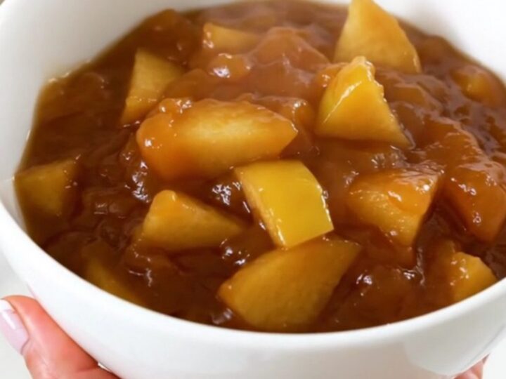 A white bowl filled with glossy, cooked quince and apple compote, showing soft, tender fruit pieces and a rich syrup.