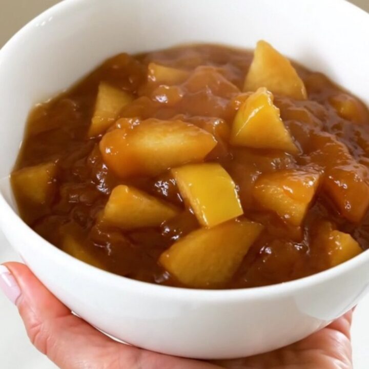 A white bowl filled with glossy, cooked quince and apple compote, showing soft, tender fruit pieces and a rich syrup.