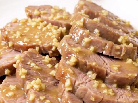 A rustic, tender pork roast served on a white plate, coated in a creamy garlic and rosemary sauce.