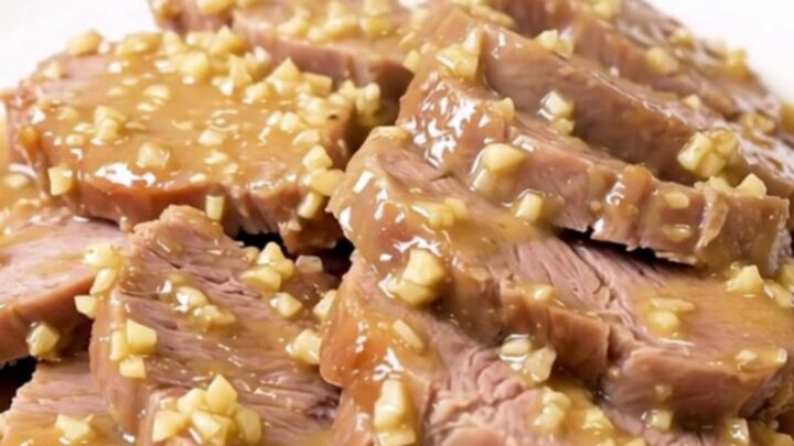 A rustic, tender pork roast served on a white plate, coated in a creamy garlic and rosemary sauce.