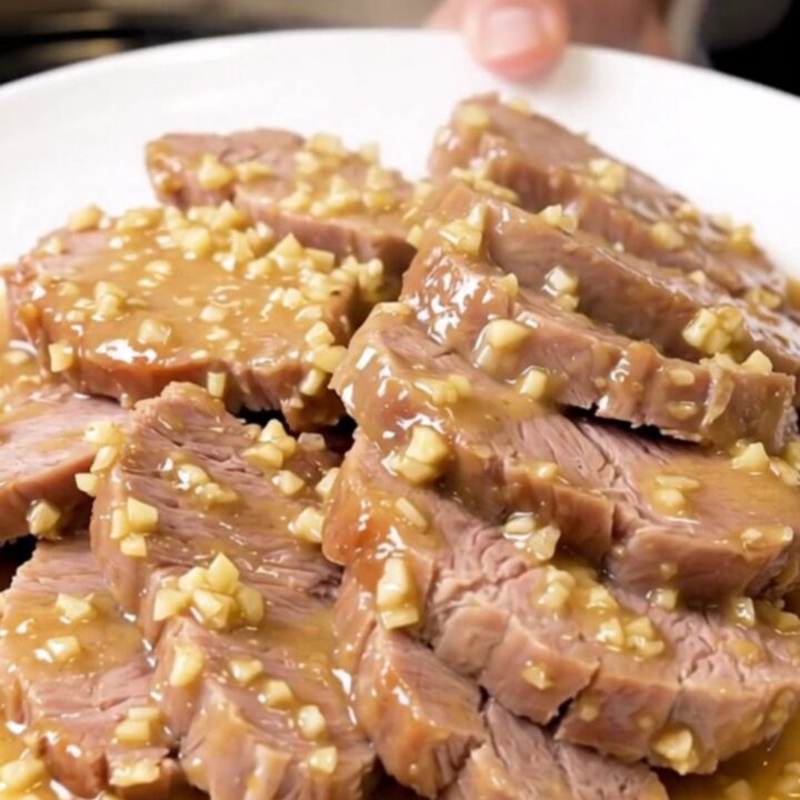 A rustic, tender pork roast served on a white plate, coated in a creamy garlic and rosemary sauce.