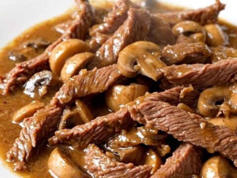 Vue de dessus d'un bœuf Stroganoff crémeux servi dans une assiette blanche, avec une sauce brillante.