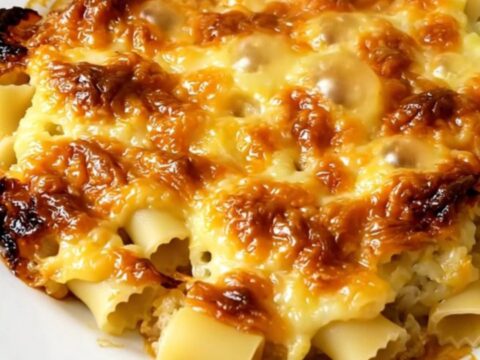 A top-down view of a black slow cooker filled with creamy crozet pasta, leeks, and melted Beaufort cheese.