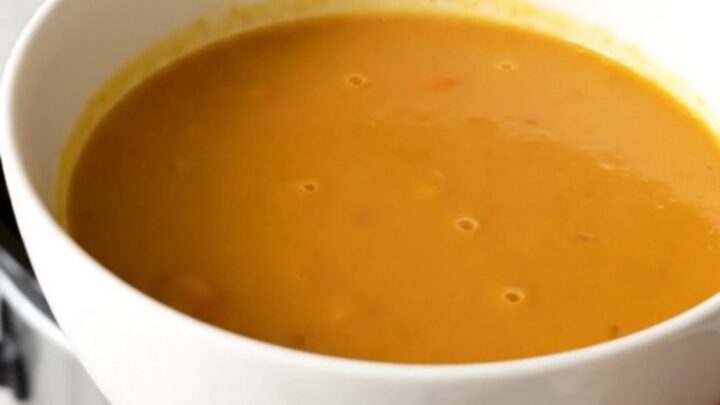 A bowl of vibrant, smooth orange curried sweet potato and carrot soup in a white ceramic bowl.
