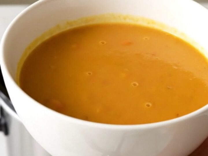 A bowl of vibrant, smooth orange curried sweet potato and carrot soup in a white ceramic bowl.