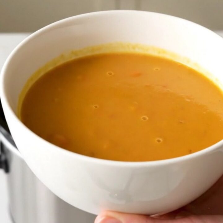 A bowl of vibrant, smooth orange curried sweet potato and carrot soup in a white ceramic bowl.